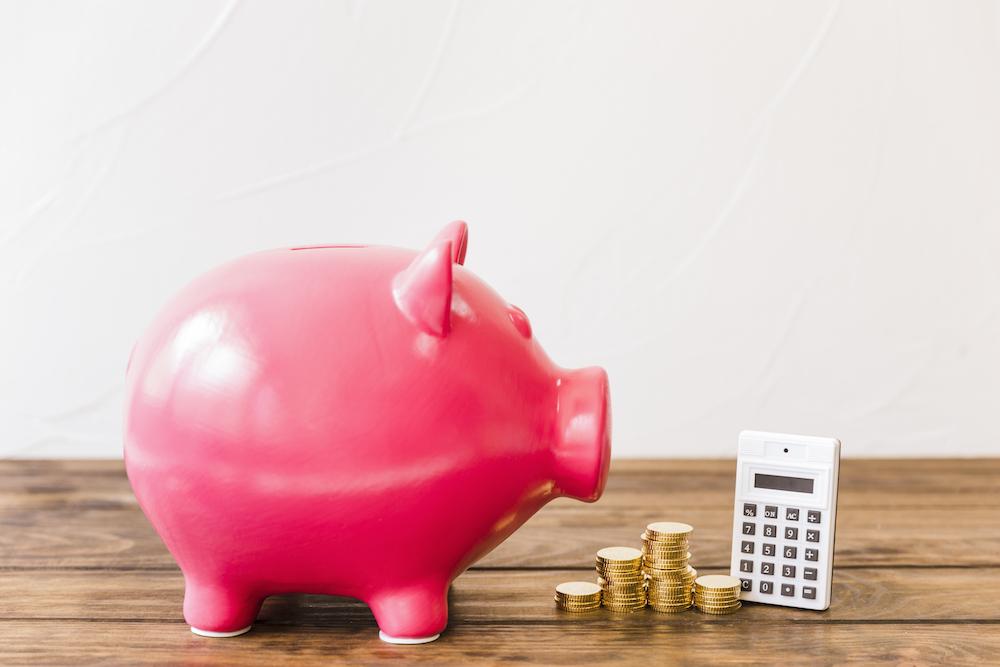 Pink piggybank besides calculator and stacked coins on wooden surface